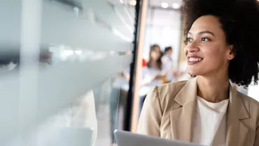 Personne souriante au bureau, tenant un ordinateur portable.