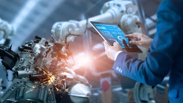 Personne utilisant une tablette pour contrôler un bras robotique en usine.