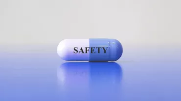 Pilule bicolore avec le mot 'SAFETY' posé sur surface bleue.
