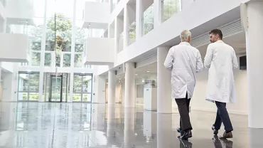 Deux personnes en blouses blanches marchent dans un hall moderne et lumineux.