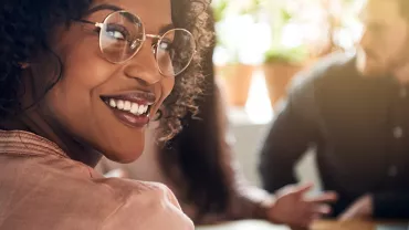 Personne souriante avec des lunettes dans un bureau lumineux.