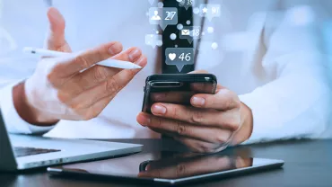 Personne utilisant un smartphone avec des icônes de médias sociaux flottantes.