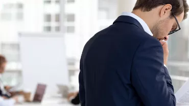 Personne en costume lisant des documents dans un bureau.