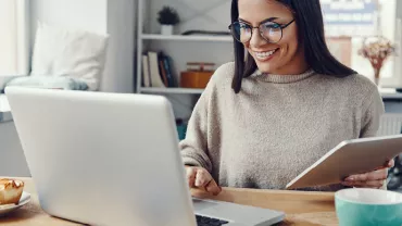 Personne souriante travaillant sur un ordinateur portable avec une tablette.