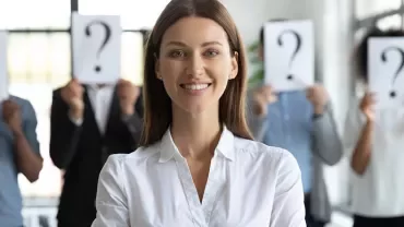 Personne souriante au premier plan, autres avec pancartes point d'interrogation en arrière-plan.