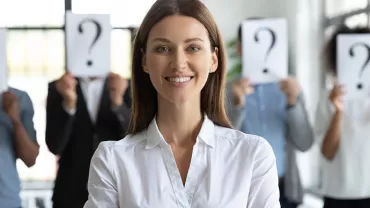 Personne souriante au premier plan, autres avec pancartes point d'interrogation en arrière-plan.