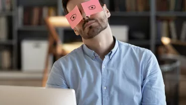 Personne assise à un bureau avec des notes autocollantes sur les yeux.