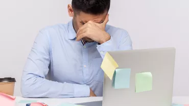 Personne avec la tête baissée devant un ordinateur portable.