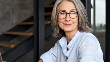 Personne souriante avec des lunettes, assise à une table.