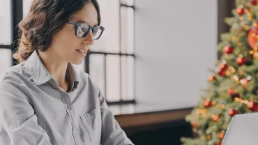 Personne travaillant sur un ordinateur portable près d'un sapin de Noël.