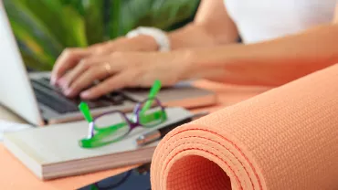 Personne tapant sur un ordinateur portable à côté d'un tapis de yoga et de lunettes.