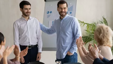 Réunion d'affaires, deux personnes debout souriantes, autres applaudissant.