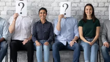 Groupe de personnes assises, certains cachant leur visage avec un point d'interrogation.