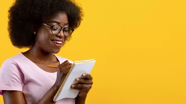 Personne souriante écrivant dans un carnet sur fond jaune.