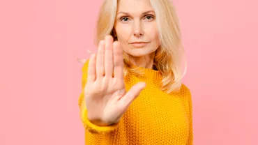 Personne en pull jaune tendant la main sur fond rose.