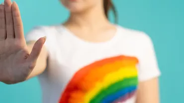 Personne vêtue d'un t-shirt arc-en-ciel levant la main.