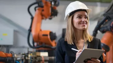 Personne avec un casque tenant une tablette dans une usine avec des robots.