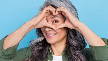 Personne souriante avec les mains formant un cœur devant les yeux.