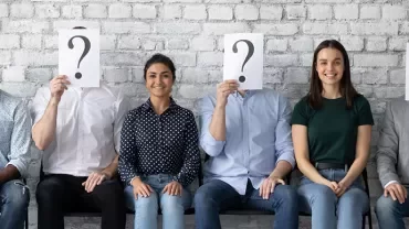 Groupe de personnes assises, trois cachent leurs visages avec un point d'interrogation.