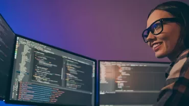 Personne souriante devant plusieurs écrans d'ordinateur avec des lignes de code.