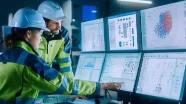 Travailleurs en usine analysant des données sur plusieurs écrans d'ordinateur.