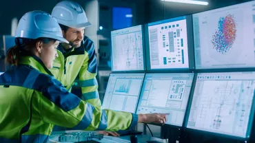 Travailleurs en usine analysant des données sur plusieurs écrans d'ordinateur.