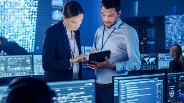 Des personnes travaillent dans un centre de surveillance informatique, entourées d'écrans affichant des données.