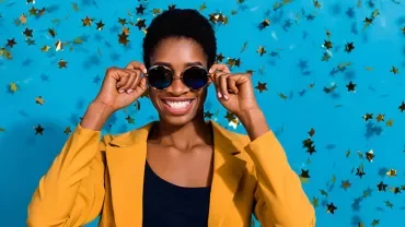 Personne souriante avec des lunettes de soleil devant un fond bleu et des étoiles dorées.
