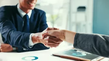 Poignée de mains entre un recruteur et un candidat dans un bureau neutre. Ambiance accord professionnel, tenues business.