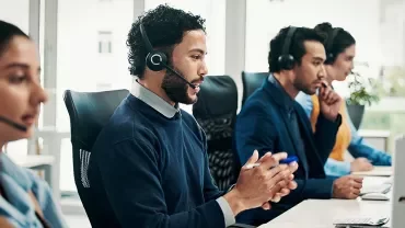 4 personnes dans un open space face à un ordinateur et au téléphone