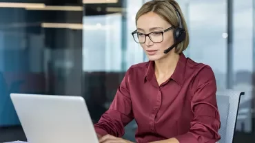 Femme souriante avec un casque micro ou échangeant de façon dynamique devant un écran.