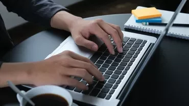 Plan rapproché sur les mains tapant sur un clavier d'ordinateur, tasse de café à côté.