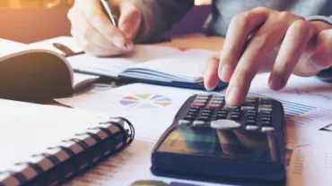 Personne utilisant une calculatrice et écrivant sur des documents.