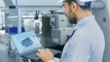 Personne en casque travaillant sur un ordinateur portable dans une usine.