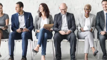 Groupe de personnes assises sur des chaises devant un mur blanc.