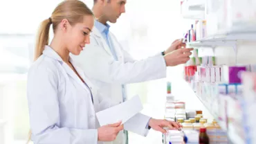 Deux personnes en blouse blanche rangent des médicaments sur des étagères.