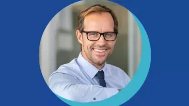 Personne souriante portant des lunettes et une chemise bleue.
