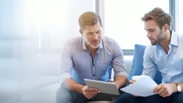 Deux personnes discutent en regardant une tablette.