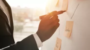 Personne écrivant sur un tableau avec des post-it.