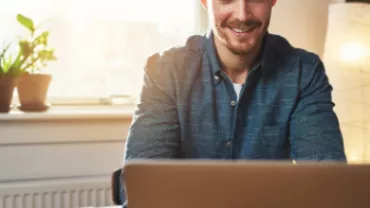 Personne souriante devant un ordinateur portable, lumière naturelle.