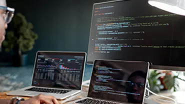 Personne travaillant sur des ordinateurs avec du code affiché sur l'écran.