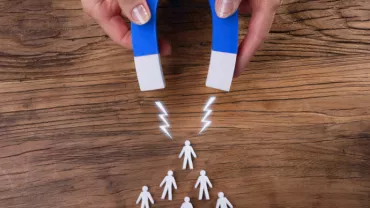 Aimant attirant des silhouettes humaines en plastique sur une table en bois.