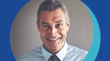 Personne souriante en chemise bleue et cravate à pois.