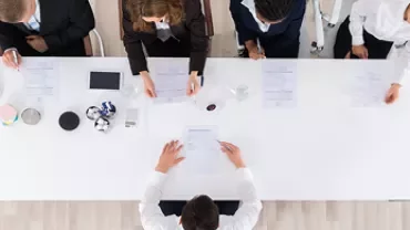 Vue aérienne d'une réunion avec plusieurs personnes assises autour d'une table blanche.