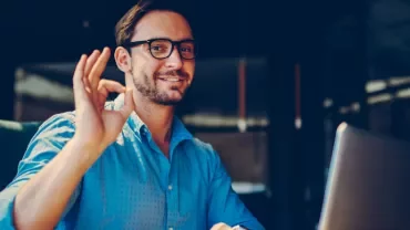 Personne souriant faisant un signe OK devant un ordinateur portable.