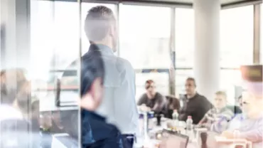 Réunion de travail dans une salle vitrée avec plusieurs personnes attentives.