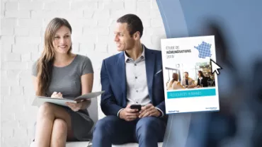 Deux personnes discutant, tenant des documents et un ordinateur portable.