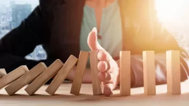 Main arrêtant des dominos en chute sur une table.