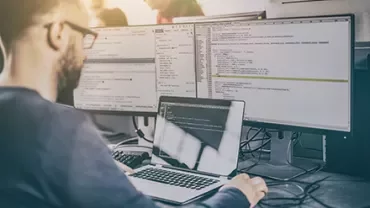 Personne utilisant un ordinateur avec plusieurs écrans affichant du code.