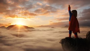 Personne en cape sur une montagne, lever du soleil sur un ciel nuageux.